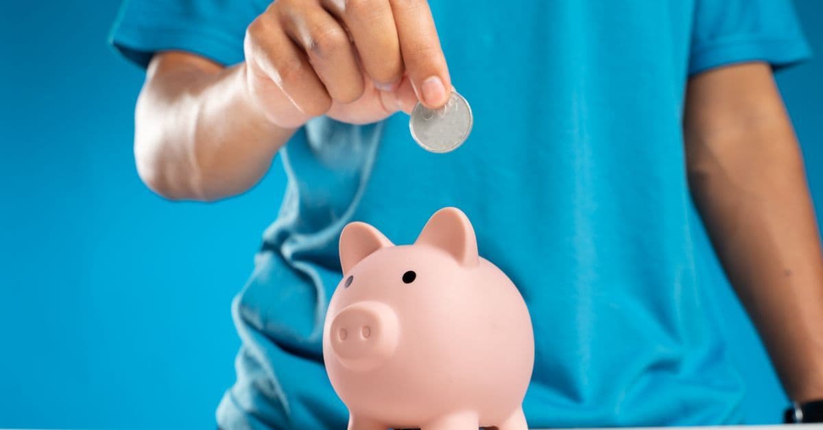 Hand wirft eine Münze in ein Sparschwein als Zeichen fürs Sparen