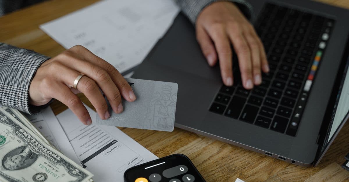 Person nutzt Kreditkarte und Laptop neben Bargeld und Taschenrechner in finanzieller Umgebung