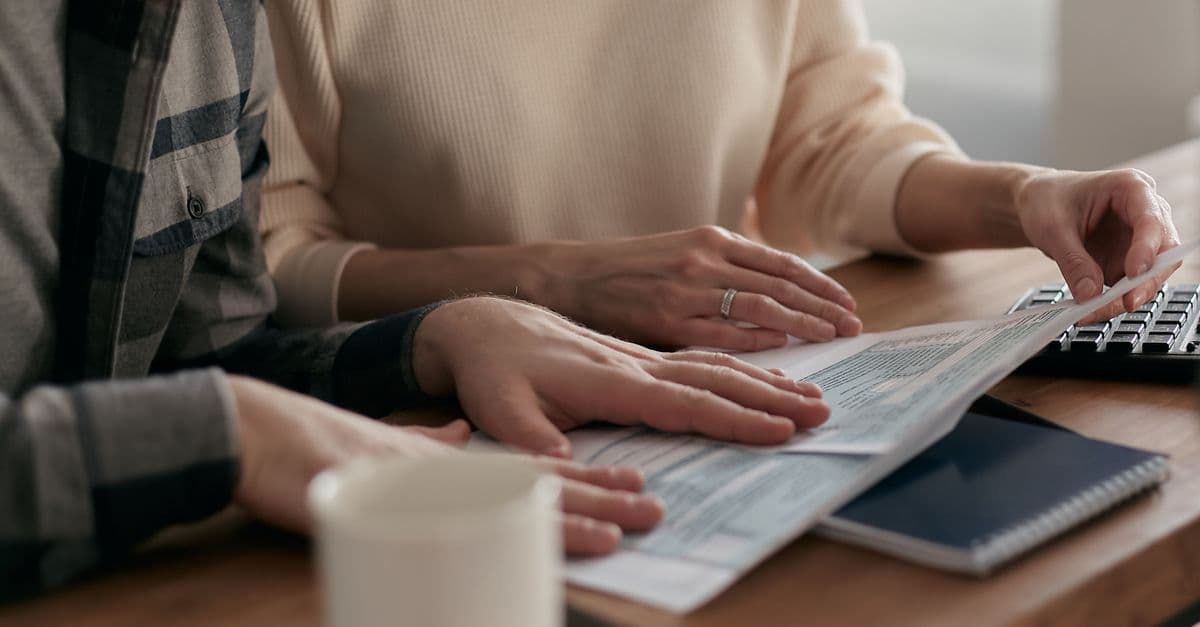 Mann und Frau prüfen Finanzunterlagen an einem Holztisch mit Tastatur und Kaffeebecher.