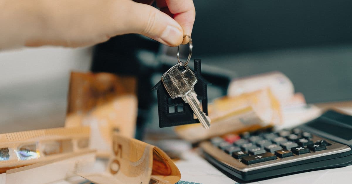 Hand mit Schlüsseln über Euro-Scheinen und Taschenrechner beim Immobilienkauf