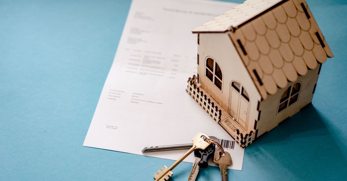 Miniatur-Holzhaus mit Schlüsseln auf einem Vertrag zum Immobilienkauf