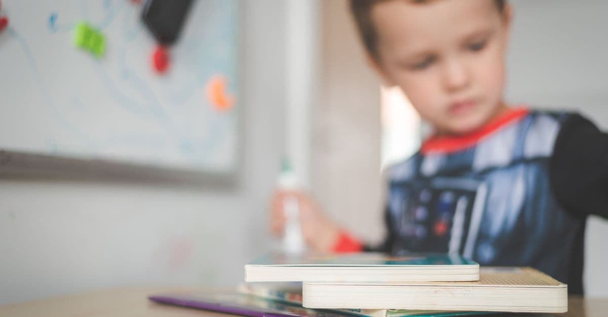 Junger Junge sitzt konzentriert an einem Schultisch und arbeitet mit mehreren Büchern.