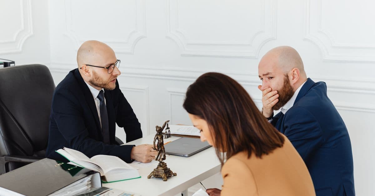 Drei Erwachsene in ernstem Beratungsgespräch in einem professionellen Büro.