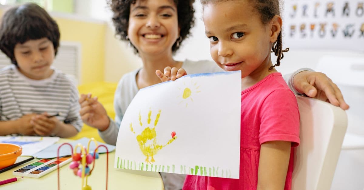 Kinder malen mit einer Lehrkraft in einem fröhlichen Klassenraum kreativ zusammen.