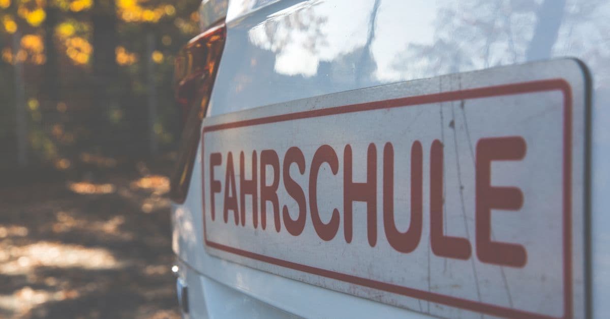 Weiße Fahrschule von der Seite, draußen vor herbstlichen Bäumen.