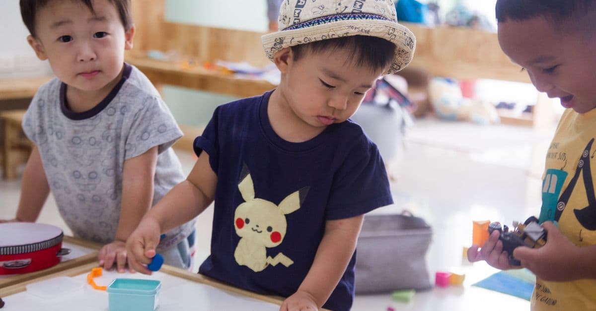 Drei kleine Kinder spielen drinnen kreativ mit Spielzeug und Malutensilien.