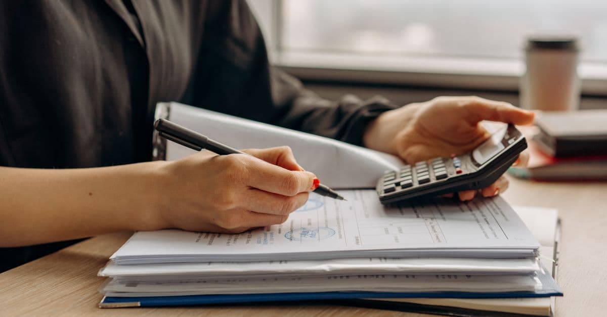 Nahaufnahme einer Person mit Taschenrechner und Finanzunterlagen im Büro.