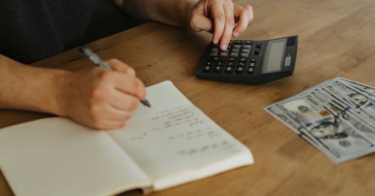 Hände mit Taschenrechner, Notizbuch und Bargeld auf einem Holztisch