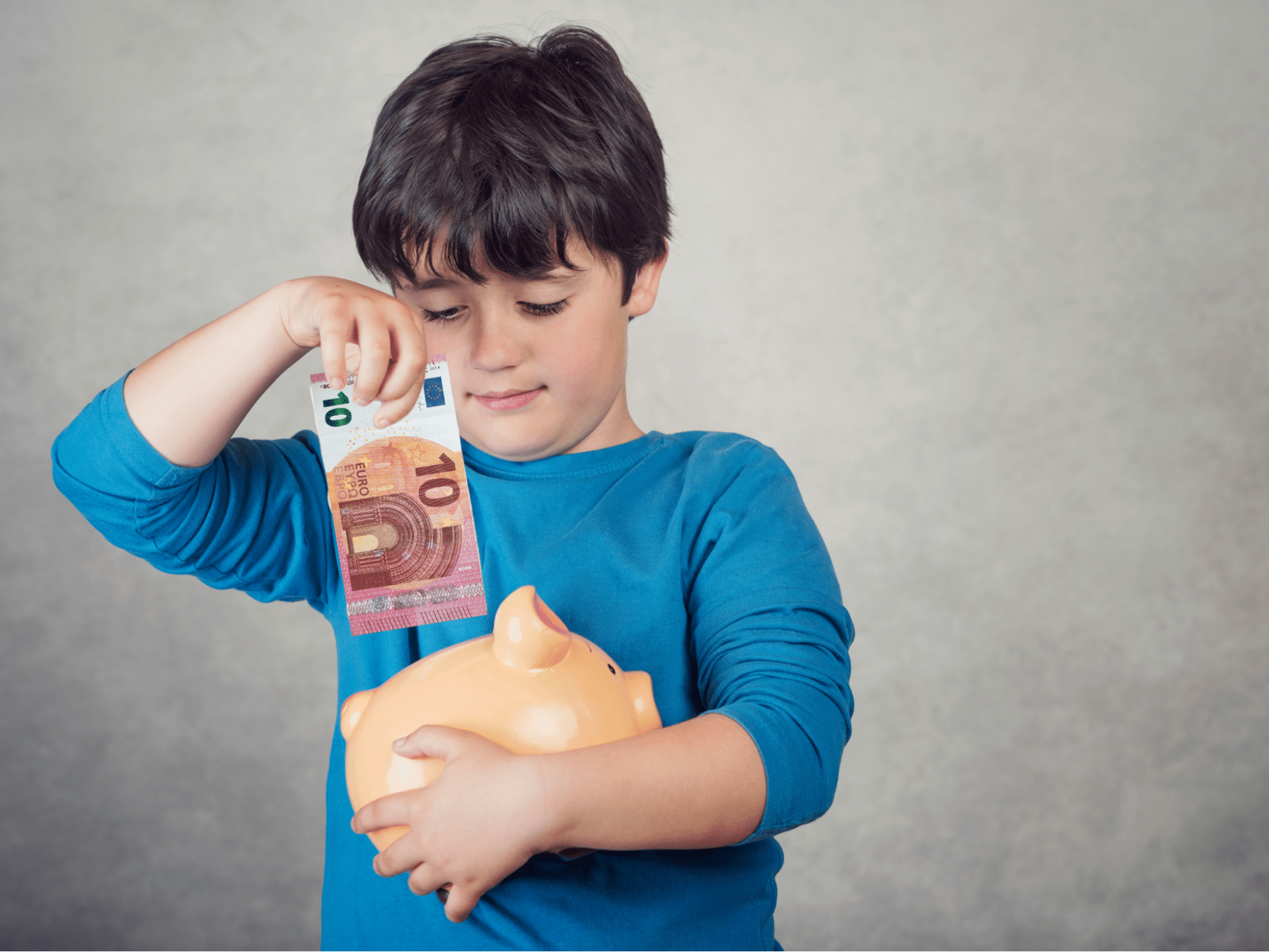 Kind steckt einen 10-Euro-Schein in ein Sparschwein.